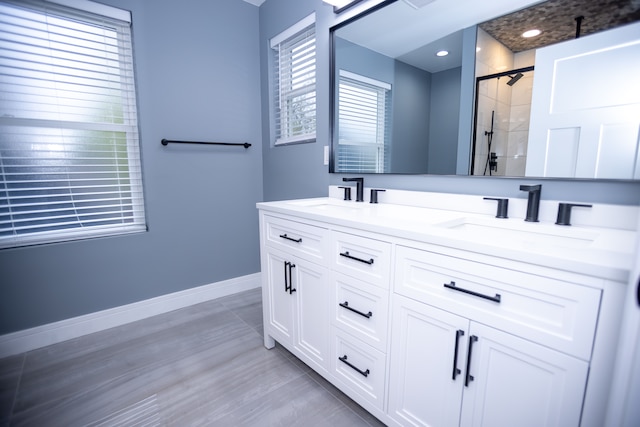 bathroom with a shower stall, baseboards, double vanity, and wood finished floors
