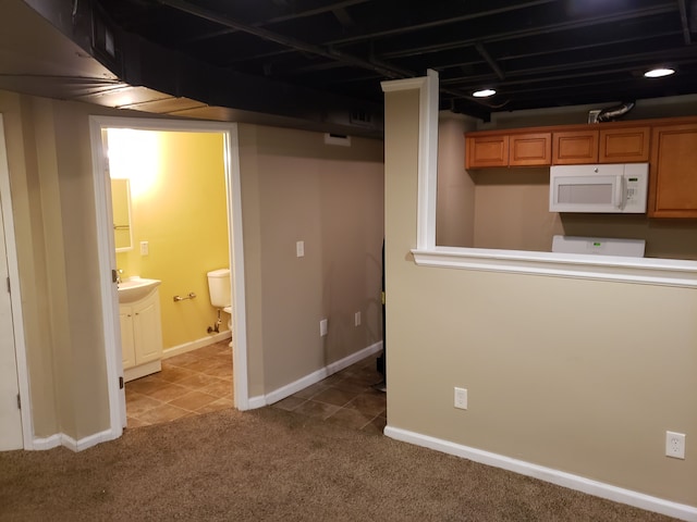 finished below grade area featuring tile patterned flooring, carpet floors, baseboards, and a sink
