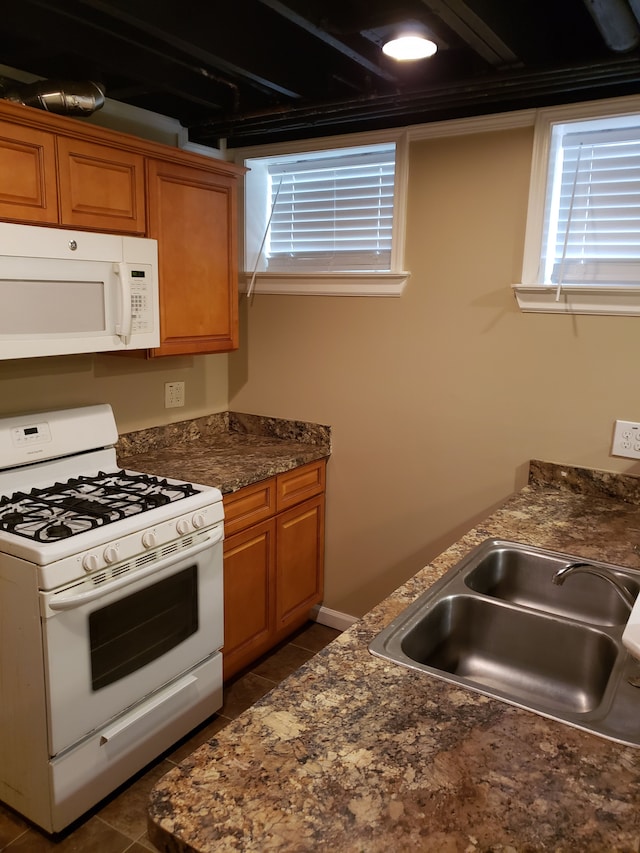kitchen featuring white appliances, brown cabinetry, a sink, and dark countertops