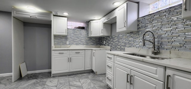 kitchen featuring a sink, backsplash, light countertops, white cabinets, and light marble finish flooring
