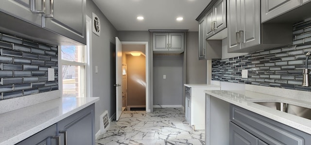 kitchen with gray cabinetry, decorative backsplash, recessed lighting, baseboards, and a sink