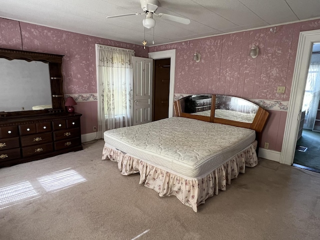 bedroom with wallpapered walls, multiple windows, wainscoting, carpet, and ceiling fan