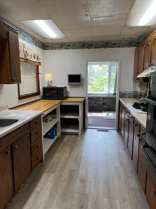 kitchen featuring black microwave, white gas stovetop, light wood-type flooring, light countertops, and under cabinet range hood