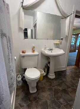 full bathroom featuring stone finish floors, toilet, and curtained shower