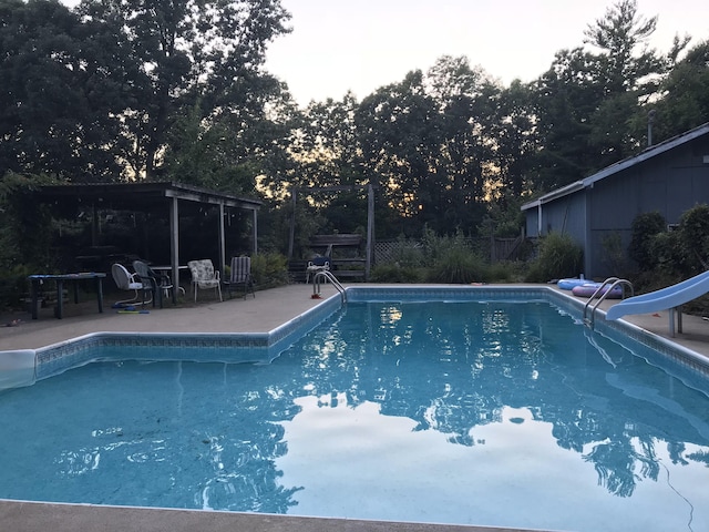 swimming pool with a water slide, a patio area, and fence