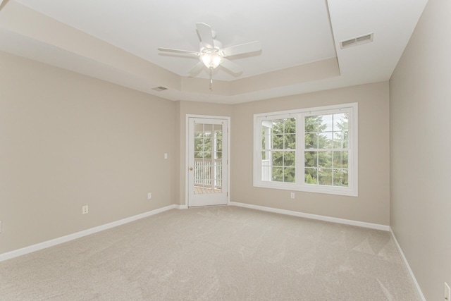 empty room with ceiling fan, light carpet, baseboards, and a raised ceiling