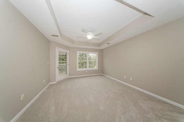 spare room with a raised ceiling, ceiling fan, baseboards, and light carpet