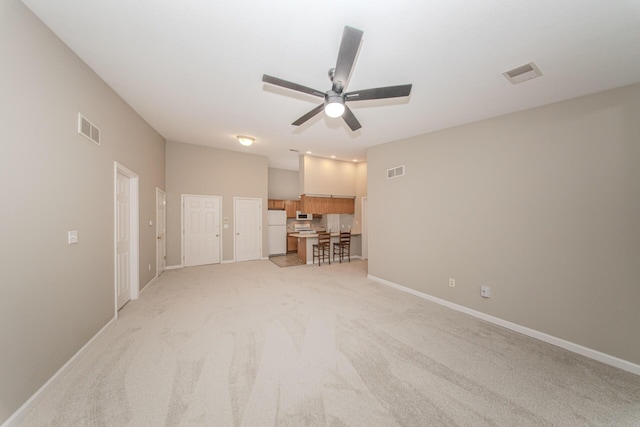 unfurnished living room with a ceiling fan, light carpet, and baseboards