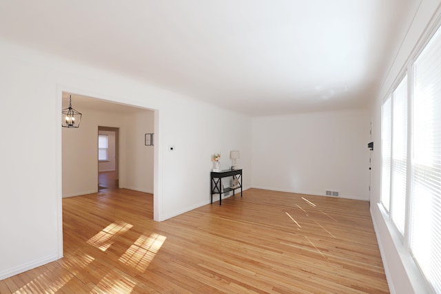 unfurnished room with a chandelier, light wood-type flooring, and baseboards