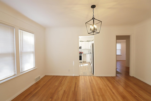 spare room with a chandelier, light wood-style flooring, and baseboards