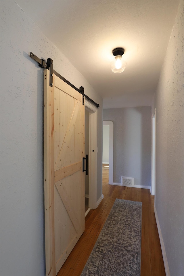 corridor with a barn door, wood finished floors, and baseboards