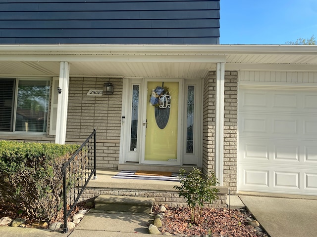 view of exterior entry featuring brick siding, a porch, and an attached garage