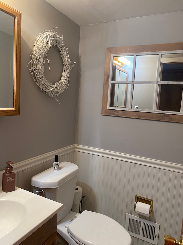half bathroom with wainscoting, toilet, and vanity