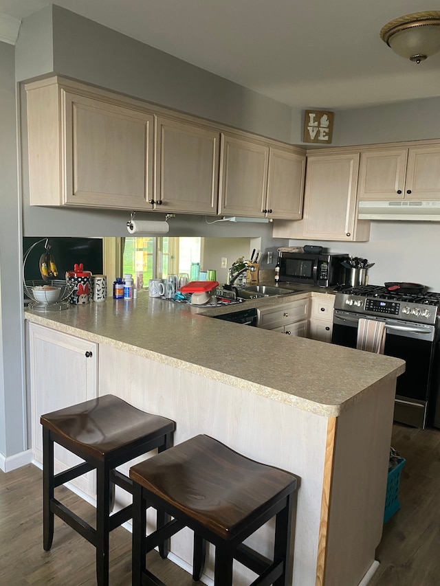 kitchen with stainless steel gas range, under cabinet range hood, black microwave, light brown cabinetry, and a peninsula