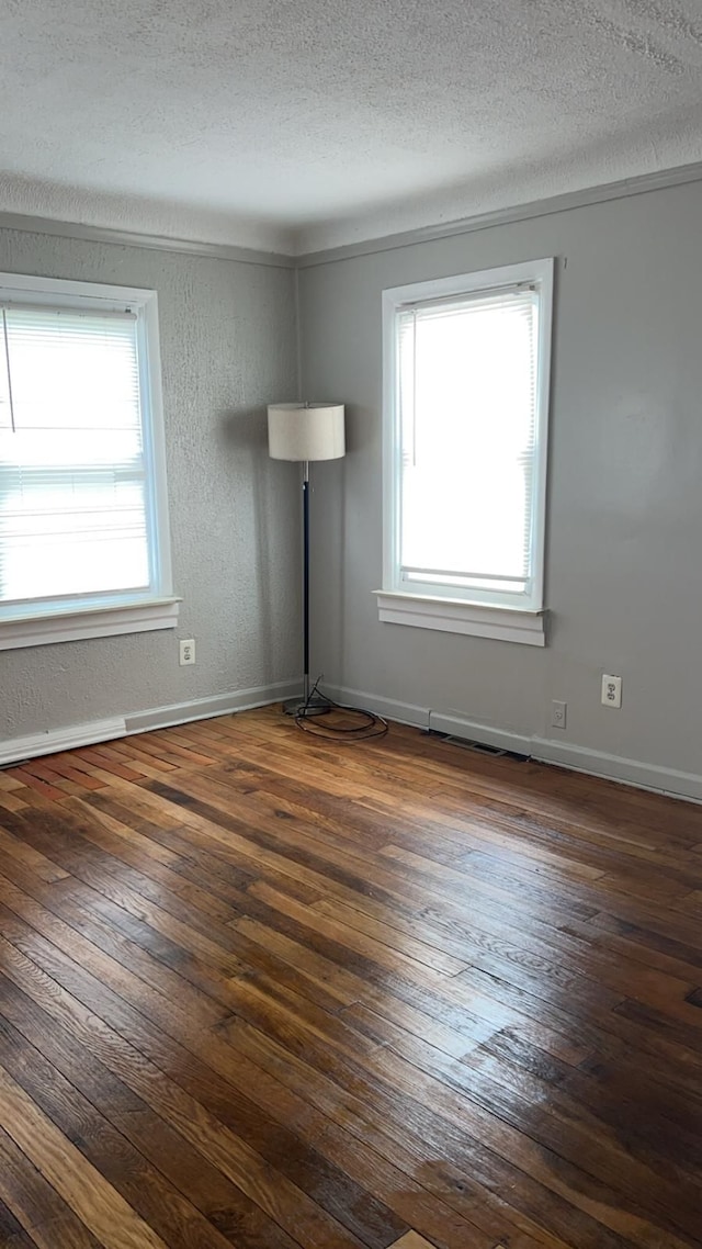 empty room featuring plenty of natural light, dark wood-style flooring, a textured ceiling, and baseboards