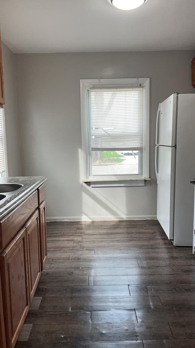 kitchen with freestanding refrigerator, baseboards, dark wood-type flooring, and brown cabinetry