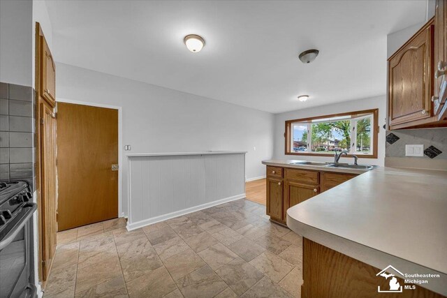 kitchen with gas range, a sink, brown cabinets, and light countertops