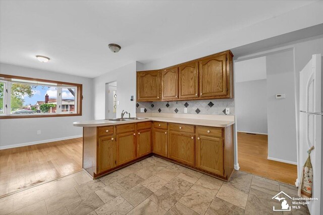 kitchen featuring a sink, brown cabinetry, light countertops, and a peninsula