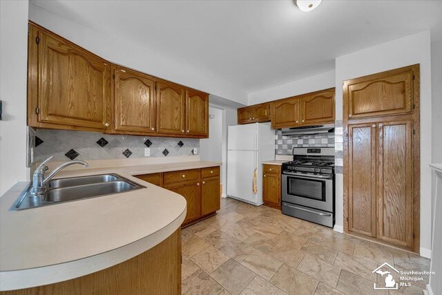 kitchen featuring gas stove, freestanding refrigerator, a sink, under cabinet range hood, and tasteful backsplash