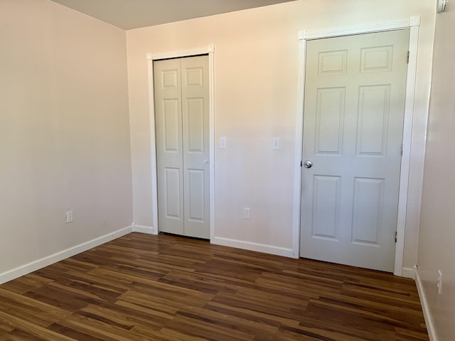 unfurnished bedroom with dark wood-style flooring, baseboards, and a closet