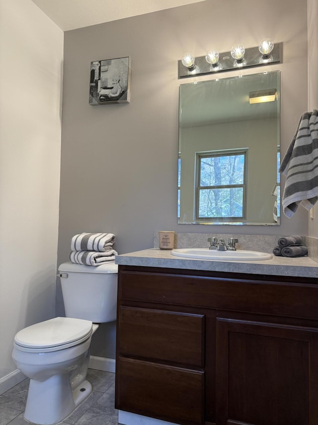 half bathroom with toilet, vanity, tile patterned floors, and baseboards