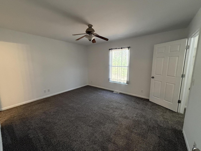 spare room featuring ceiling fan, dark carpet, and baseboards