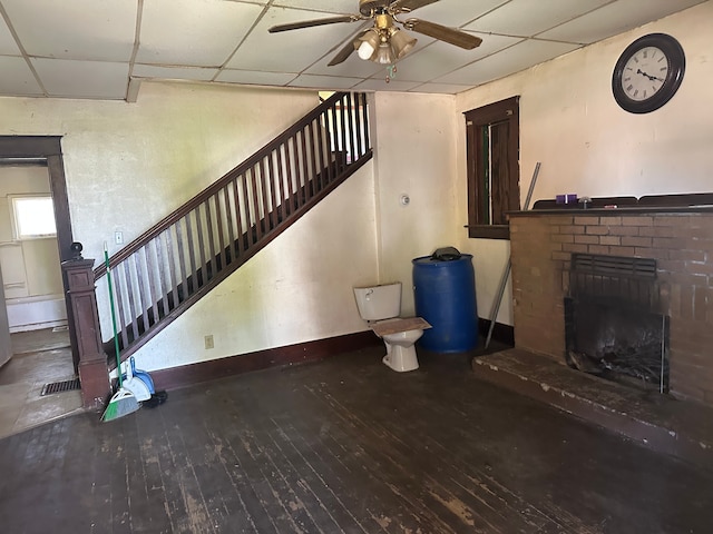 unfurnished living room with a paneled ceiling, wood-type flooring, baseboards, ceiling fan, and a fireplace