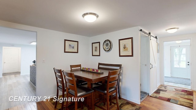 dining space featuring a barn door, wood finished floors, and baseboards