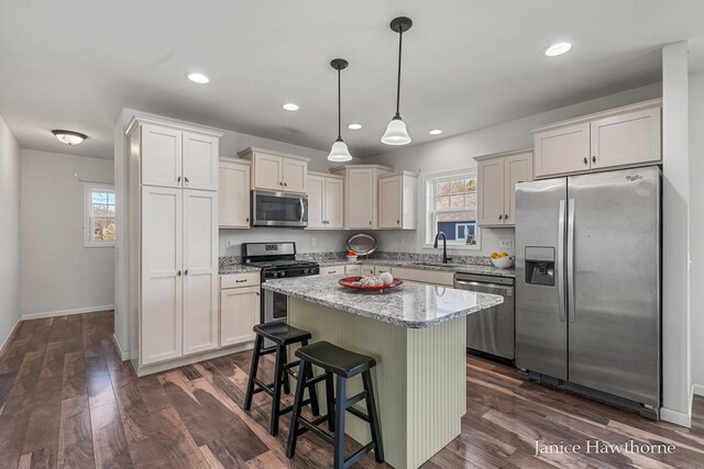 kitchen with stainless steel appliances, a sink, light stone countertops, a center island, and dark wood finished floors