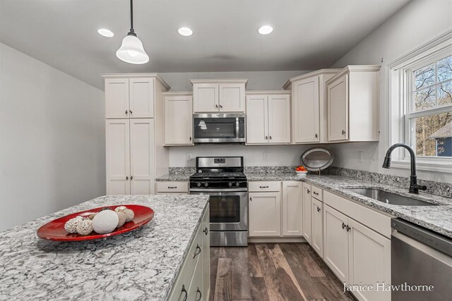 kitchen featuring stainless steel appliances, a sink, dark wood-style floors, white cabinetry, and pendant lighting