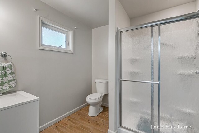 bathroom with wood finished floors, toilet, a shower stall, and baseboards