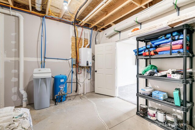 unfinished basement with a water pressure tank, a water softener system, and tankless water heater