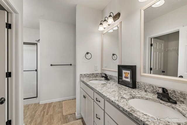 full bath featuring wood finished floors, double vanity, baseboards, and a shower
