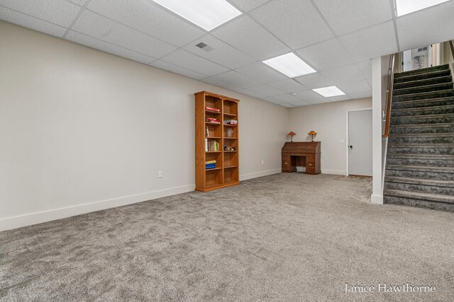 finished below grade area featuring carpet floors, stairs, a paneled ceiling, and baseboards