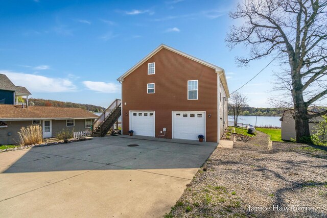 view of property exterior with stairs, a garage, concrete driveway, and a water view
