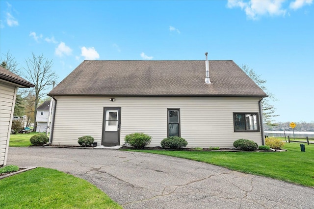 rear view of house featuring a yard and a shingled roof