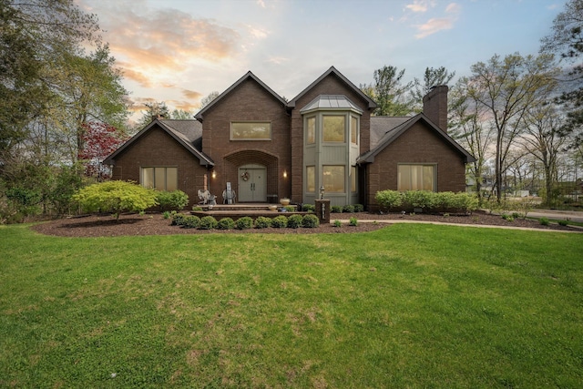 view of front of property featuring brick siding, a yard, and a chimney