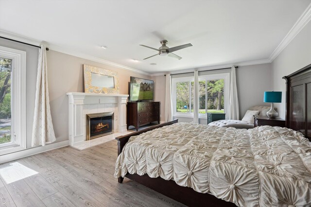 bedroom with a fireplace, multiple windows, wood finished floors, crown molding, and ceiling fan