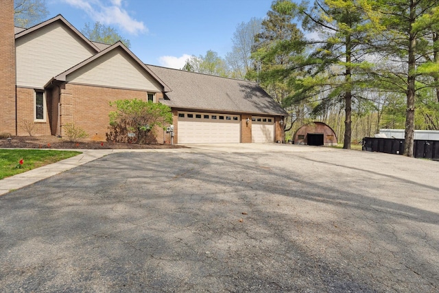 view of property exterior featuring brick siding, asphalt driveway, a garage, and a chimney