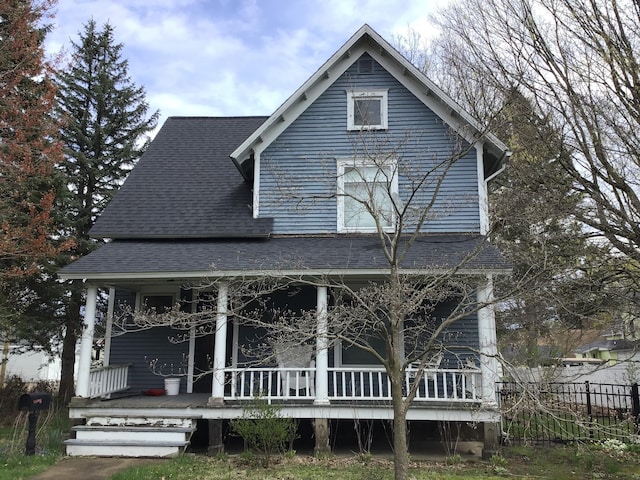 view of front facade featuring a porch, roof with shingles, and fence