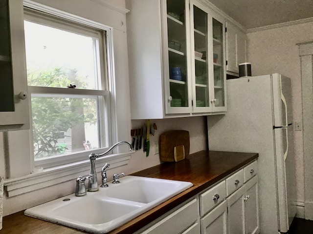 kitchen with a sink, glass insert cabinets, dark countertops, and freestanding refrigerator
