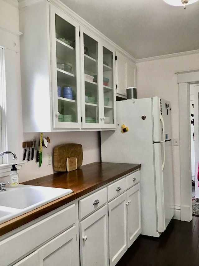 kitchen with a sink, glass insert cabinets, freestanding refrigerator, white cabinets, and crown molding