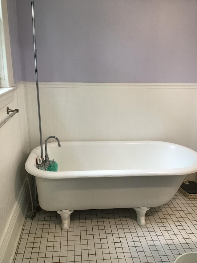 full bathroom with tile patterned floors, a wainscoted wall, and a soaking tub