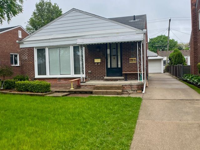 bungalow-style house with covered porch, a front yard, brick siding, and a detached garage