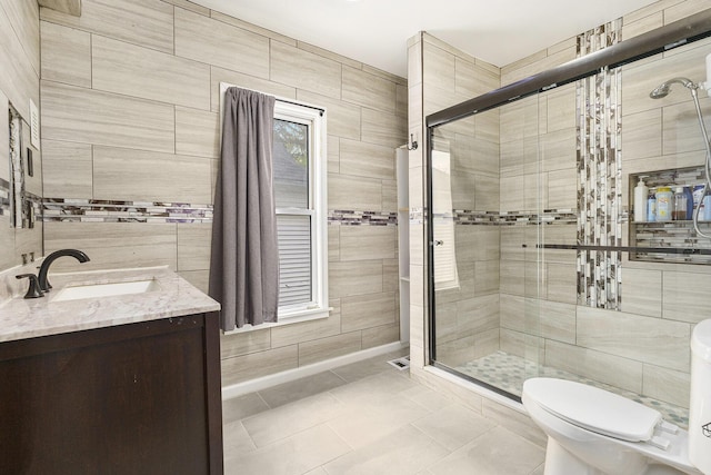 bathroom with a stall shower, tile walls, toilet, vanity, and tile patterned floors