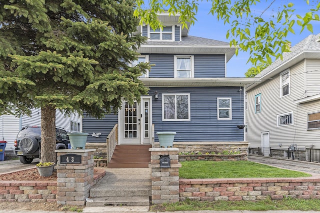 american foursquare style home featuring entry steps, fence, and a shingled roof
