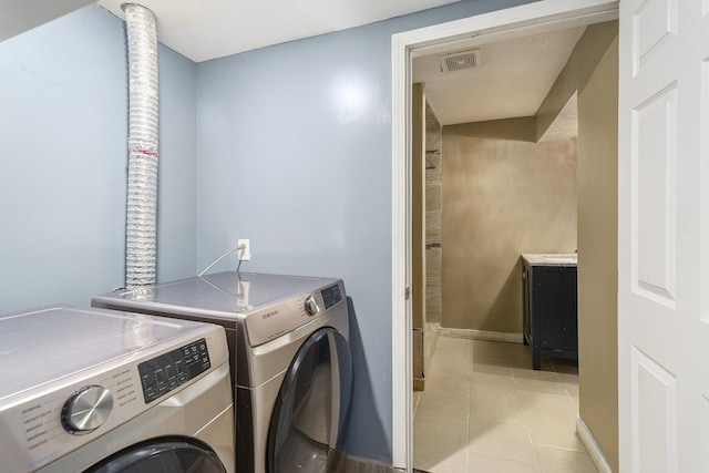 washroom featuring washing machine and dryer, light tile patterned floors, and baseboards
