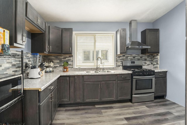 kitchen featuring stainless steel gas range oven, wall chimney exhaust hood, a sink, light countertops, and decorative backsplash