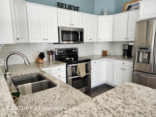 kitchen featuring stainless steel appliances, a sink, white cabinetry, and light stone counters