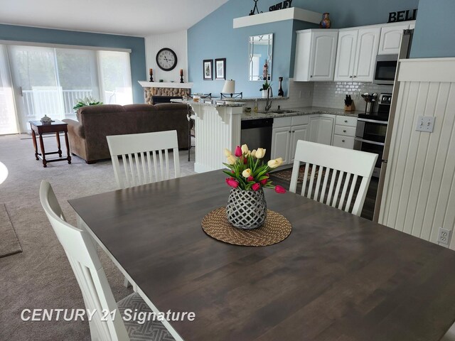 dining room with light colored carpet, vaulted ceiling, and a fireplace